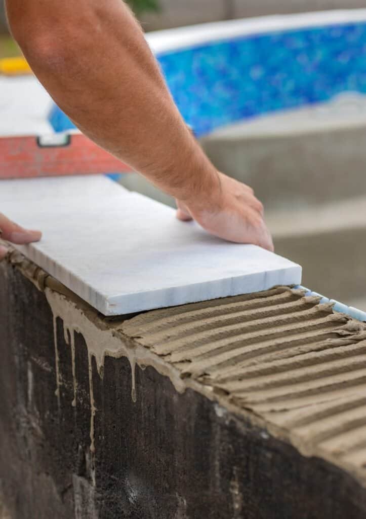 Worker installing pool coping with marble tile in Los Angeles.